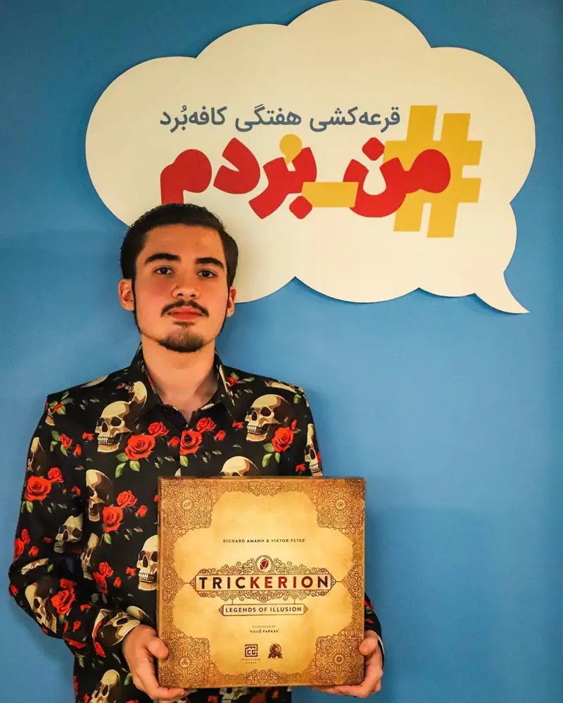 تصویری از برنده قرعه کشی هفتگی کافه برد که با خوشحالی بازی Trickerion را در دست دارد و در کنار لوگوی #من_بردم ایستاده است.