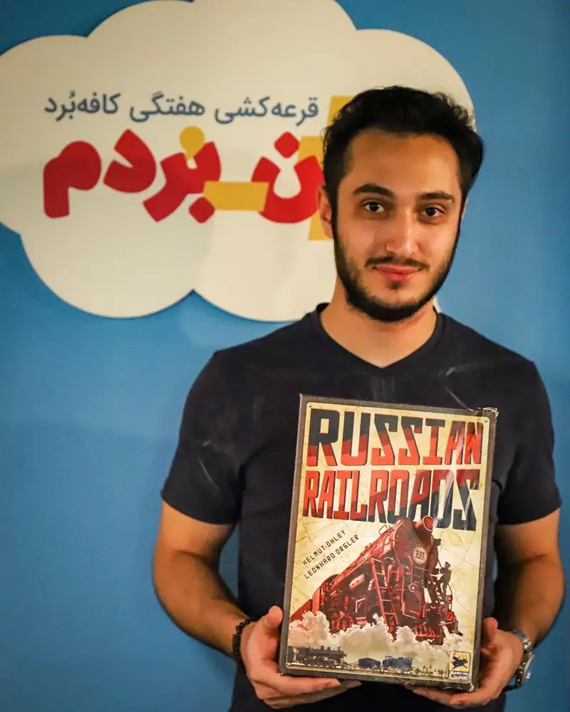 تصویری از برنده خوشحال قرعه‌کشی هفتگی کافه برد، با جایزه بازی رومیزی Russian Railroads. مناسب برای سایت فروشگاه بازی‌های فکری.