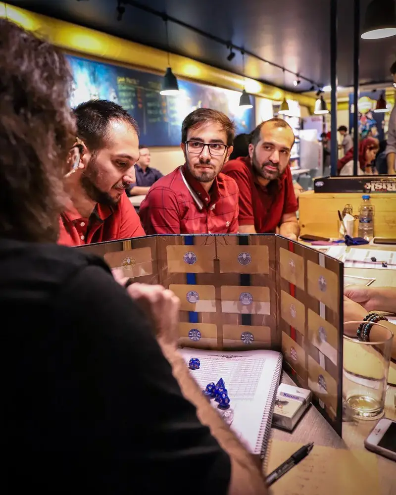 دورهمی دوستان در کافه برد، مشغول بازی رومیزی هیجان‌انگیز با تاس و دفترچه. یک تجربه جذاب برای علاقه‌مندان به بازی‌های گروهی.