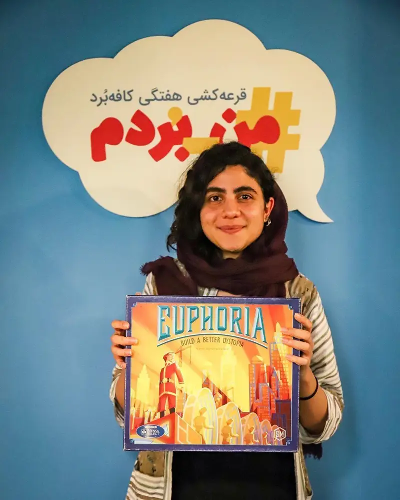 برنده خوشحال قرعه کشی هفتگی کافه برد، زن جوانی که بازی فکری Euphoria را در دست دارد. پس زمینه آبی با هشتگ #من_بردم.