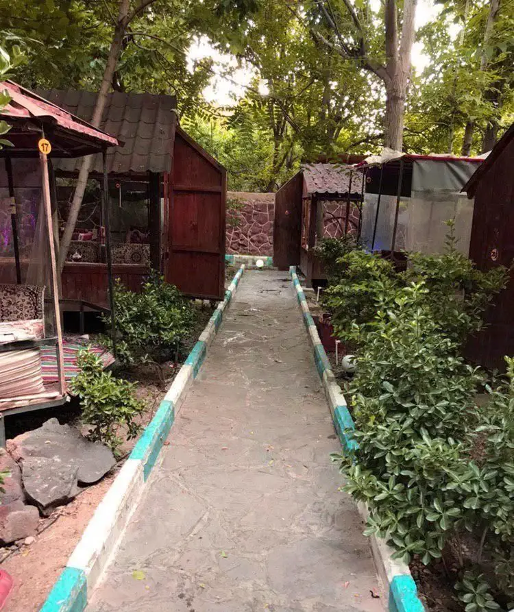 فضای سرسبز و دلپذیر رستوران ایرانی آرامیس با آلاچیق‌های چوبی مجزا، مسیر سنگفرش شده و درختان سر به فلک کشیده، ایده‌آل برای آرامش.