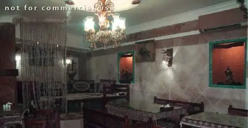 دکوراسیون داخلی رستوران ایرانی زند: لوستر کلاسیک، میز و صندلی‌های چوبی با منبت‌کاری، دیوارهای کرم و طاقچه‌های سبز.