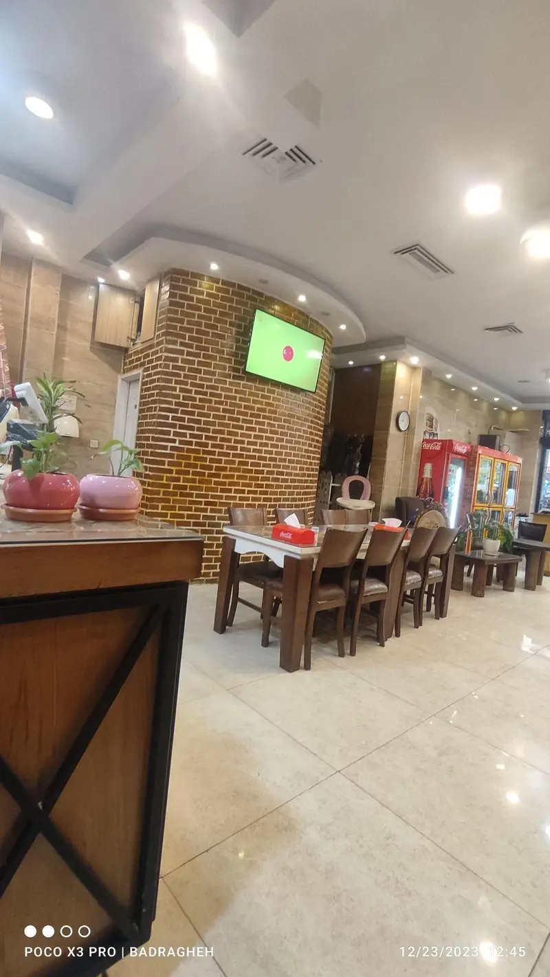 فضای داخلی فست فود کیان گریل با میز و صندلی‌های چوبی شیک، دیوارهای آجری، و تلویزیون. محیطی پاکیزه و دلنشین برای مشتریان.