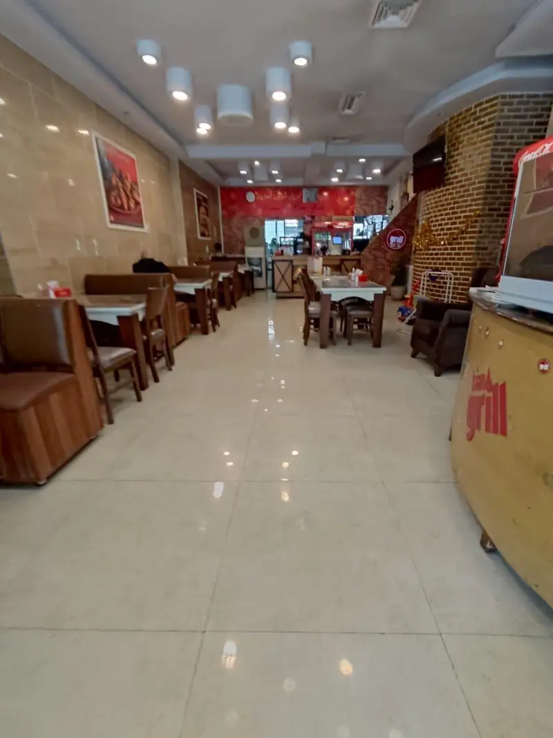 فضای داخلی وسیع و روشن فست فود کیان گریل با میز و صندلی‌های چوبی، دیوار آجری و دکوراسیون جذاب، آماده پذیرایی از مشتریان است.