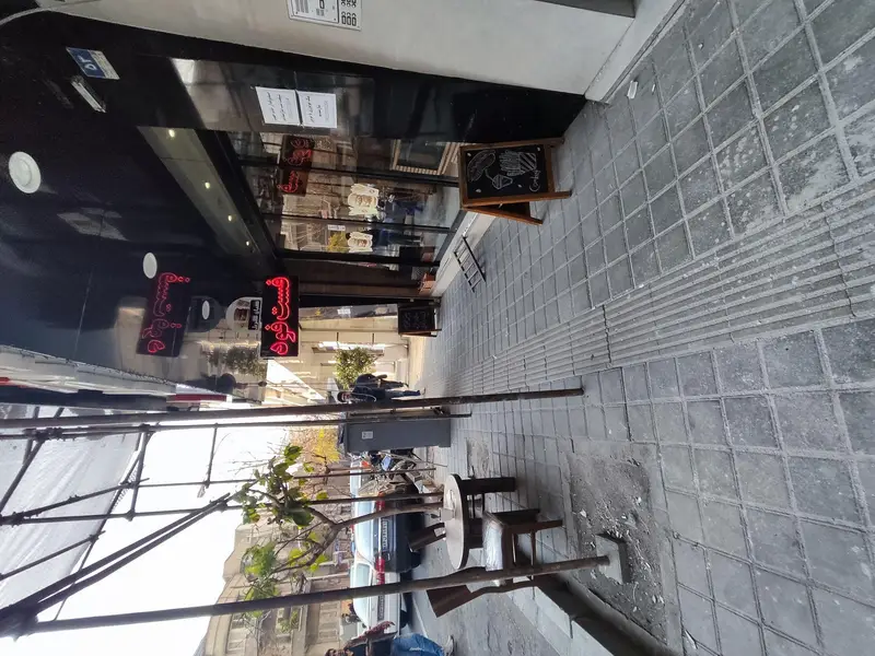 نمای بیرونی فست فود کیان گریل در روز، شامل تابلوی نئون قرمز، منوی غذا روی تخته سیاه و فضای نشیمن در پیاده رو.