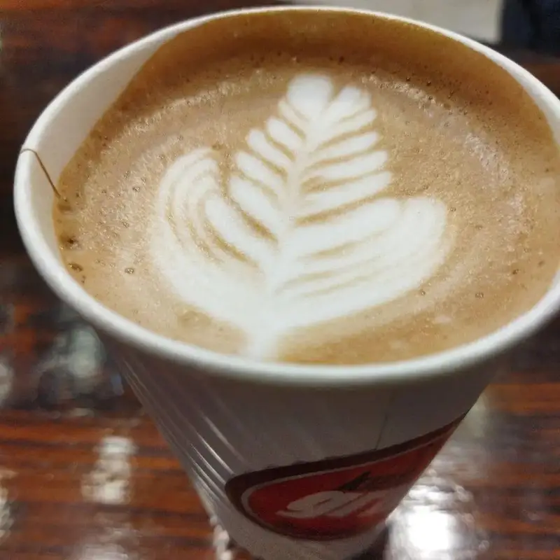 تصویری از یک فنجان قهوه لاته خوش‌طعم با لاته آرت حرفه‌ای طرح برگ، سرو شده در فست فود کیان گریل. لذت یک نوشیدنی عالی.