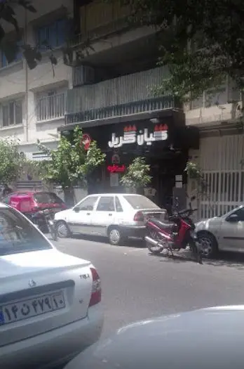 تصویری از نمای بیرونی فست فود کیان گریل در خیابان، با تابلوی مشکی و حروف برجسته سفید، و خودروهایی در حال پارک.