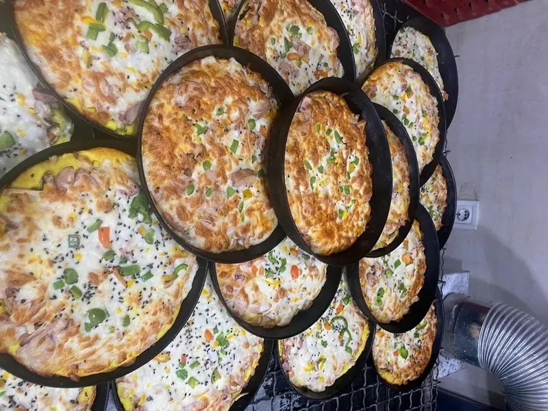 تعداد زیادی املت یا فریتاتای خوشمزه و آماده سرو با مخلفات فلفل دلمه، ذرت و سوسیس در ظروف گرد در فست فود کیان گریل.