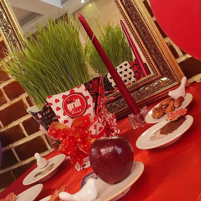 سفره هفت سین نوروزی کیان گریل، با سبزه سرسبز، سیب قرمز و شمع‌های روشن، نشان‌دهنده فضای دلنشین و جشن در فست فود کیان گریل.