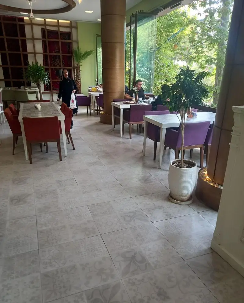 رستوران کمالی، محیطی آرام با دکوراسیون شیک، میزهای غذاخوری قرمز و بنفش، پنجره بزرگ رو به طبیعت و مشتریان در حال صرف غذا.