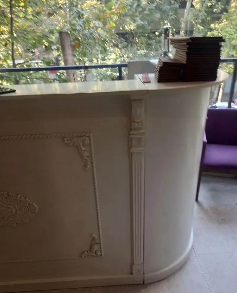 پیشخوان مجلل و سفید رنگ رستوران کمالی با منوهای آماده سرویس دهی، دکوراسیون داخلی کلاسیک و چشم‌انداز فضای سبز.