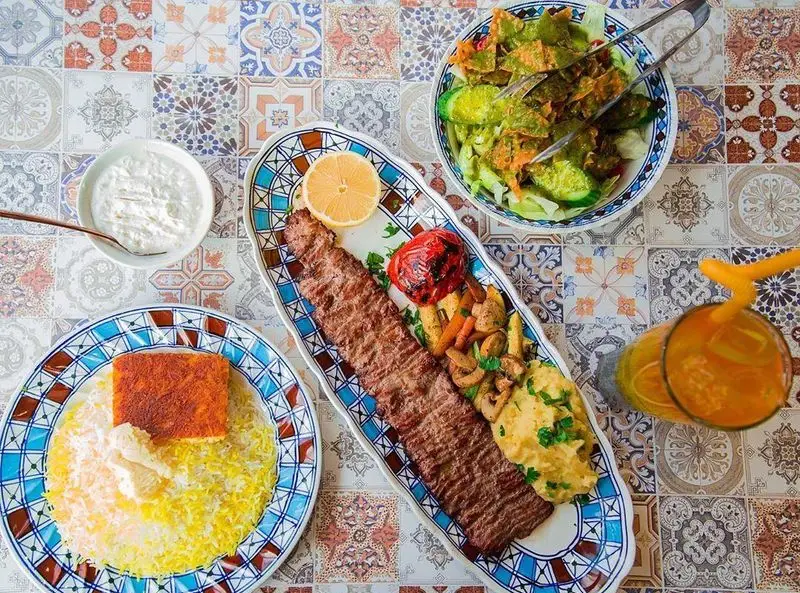 میز غذای کامل شامل چلوکباب کوبیده رستوران کمالی با ته دیگ زعفرانی، سالاد فصل و ماست برای تجربه طعم اصیل ایرانی.