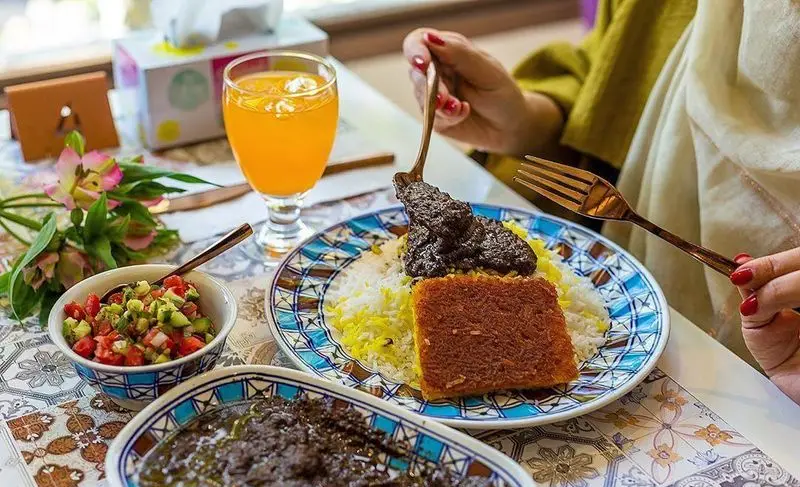 تصویری جذاب از غذای اصیل ایرانی در رستوران کمالی: برنج زعفرانی، ته دیگ طلایی، خورش و سالاد شیرازی تازه. یک تجربه ناهار ایده‌آل.
