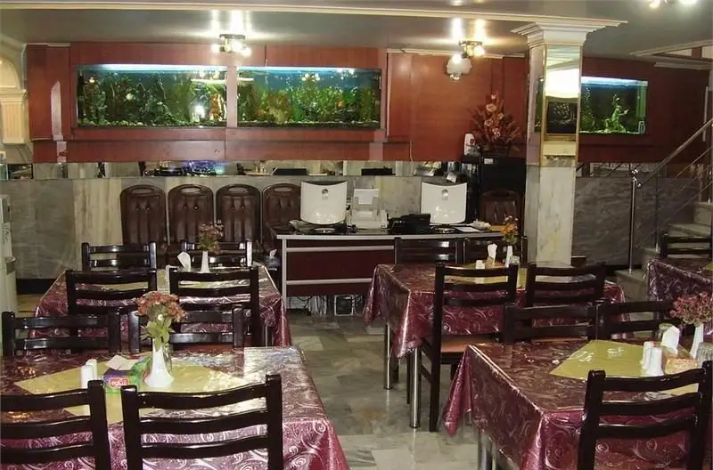 فضای داخلی رستوران ایرانی پذیرا با میز و صندلی‌های چوبی، دکوراسیون سنتی، آکواریوم‌های بزرگ و محیطی دلنشین برای صرف غذا.