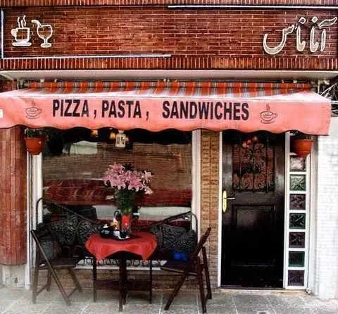 نمای بیرونی کافه و رستوران آناناس با آجرکاری شیک، آفتابگیر نارنجی دارای منوی پیتزا، پاستا، ساندویچ و میز و صندلی دنج در فضای باز.