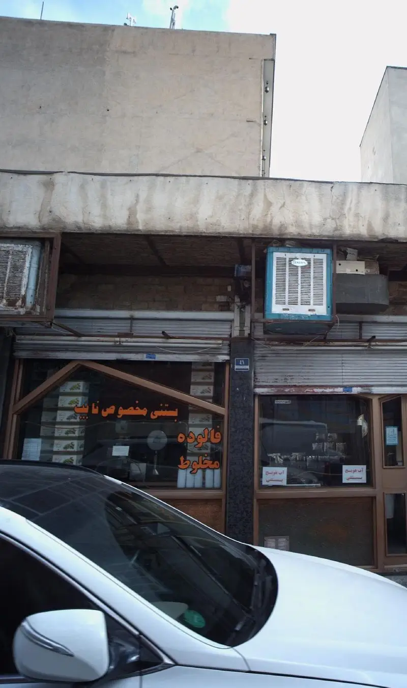 نمای بیرونی فروشگاه بستنی مخصوص نایب با تابلوی "فالوده مخلوط". یک خودروی سفید در جلوی مغازه و کولرهای آبی بالای آن دیده می‌شود.