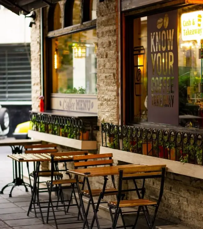 نمای بیرونی کافه کباب آرمنیا با میز و صندلی‌های چوبی برای فضای باز. تابلوی "Coffee MENU" و "KNOW YOUR COFFEE TAKEAWAY" در ویترین کافه.