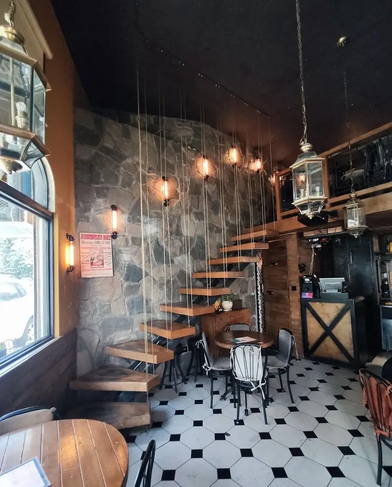 دکوراسیون داخلی کافه کباب آرمنیا با دیوار سنگی، پله چوبی معلق، فضای دنج و نورپردازی گرم با کفپوش شطرنجی.