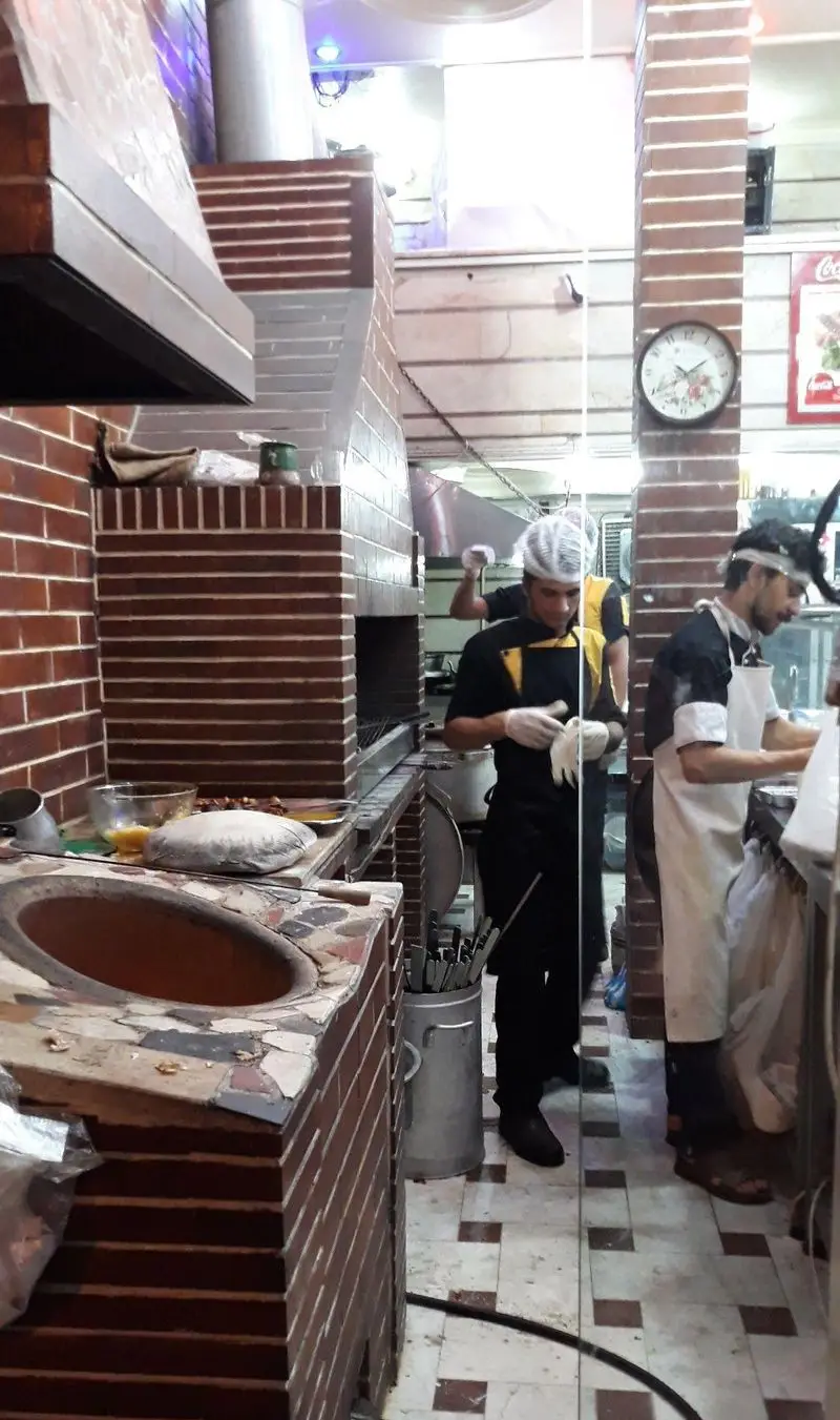 آشپزخانه فعال و سنتی کسب و کار کباب ذغالی و نان تنوری، شامل تنور و منقل، آشپزها مشغول پخت و آماده سازی غذاهای تازه.