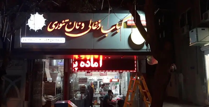 کباب ذغالی و نان تنوری، آماده پخت و سرو غذای خوشمزه ایرانی در رستورانی با تابلوهای روشن در شب.