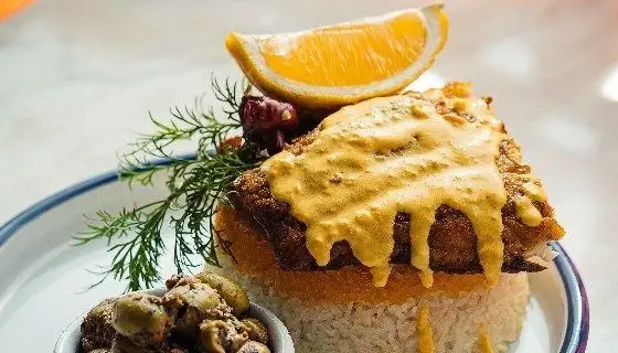 تصویری از ماهی پلو خوشرنگ با سس طلایی، تزیین پرتقال و شوید به همراه زیتون در رستوران دست. طعمی به یادماندنی از غذای سنتی ایرانی.