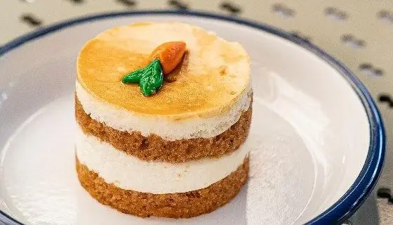 کیک هویج لذیذ و خانگی رستوران دست، با لایه‌های نرم کیک و کرم پنیری، تزئین شده با هویج مینیاتوری، انتخابی عالی برای دسر.