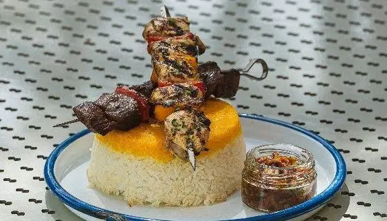 نمایی جذاب از چلوکباب لذیذ رستوران دست: کباب‌های تازه گوشت و مرغ در کنار برنج زعفرانی قالبی و سس ویژه. غذای سنتی ایرانی.
