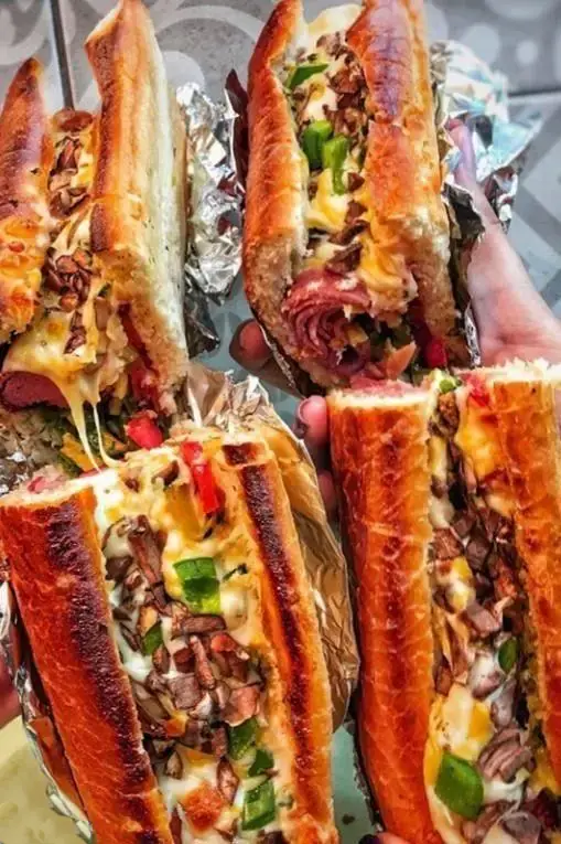 نمای نزدیک از ساندویچ‌های خوشمزه و بزرگ فست فود، با پنیر فراوان و مخلفات لذیذ گوشتی و سبزیجات، ارائه شده توسط بستنی کابانا.