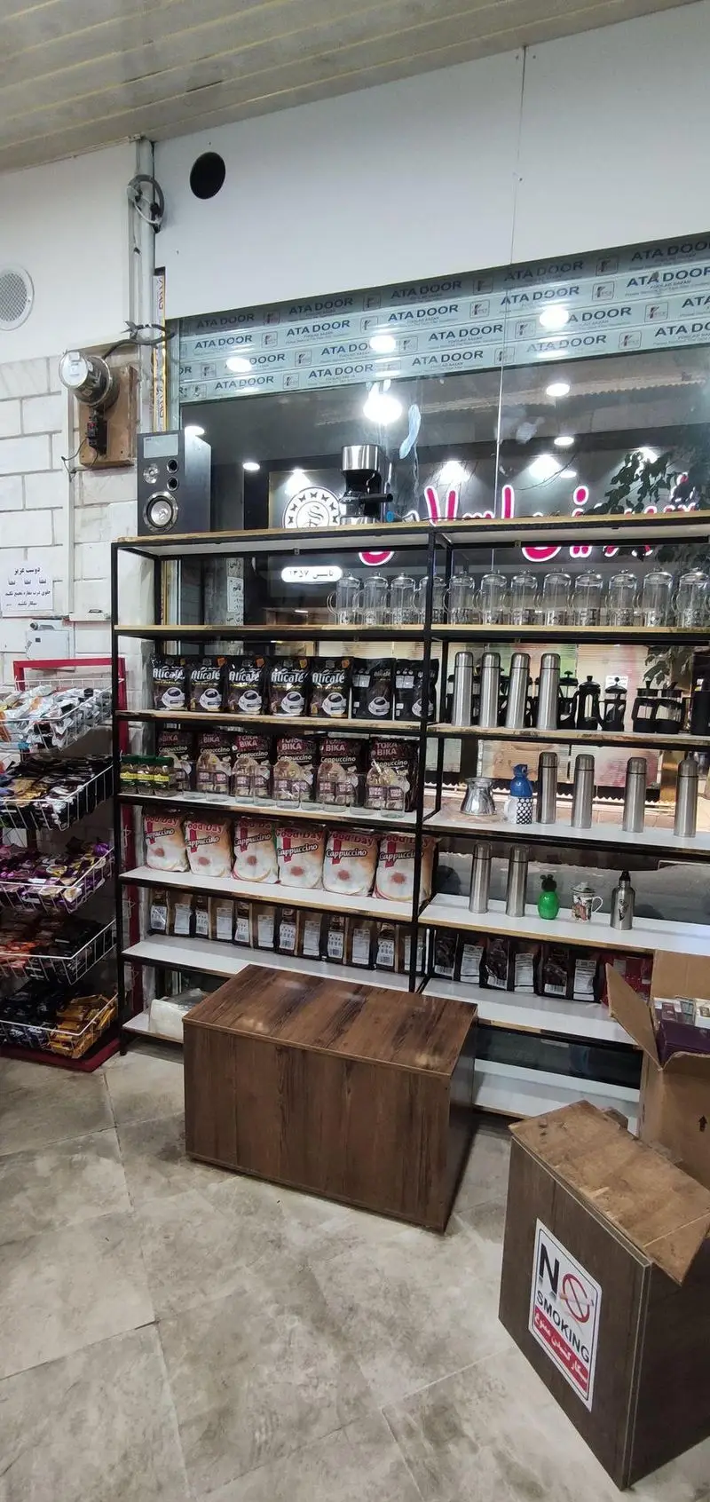کافه و قهوه کسری: نمای داخلی با قفسه‌های چوبی مملو از محصولات قهوه، قهوه‌ساز و لوازم جانبی. محیطی دلنشین برای خرید و تجربه قهوه.