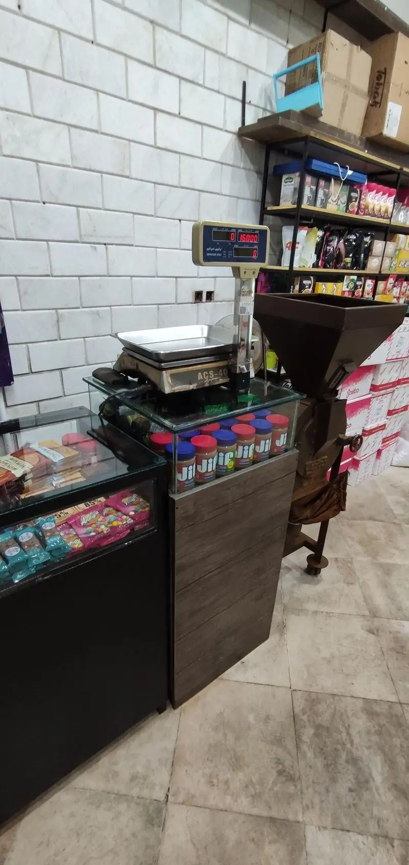 فضای داخلی کافه و قهوه کسری با ترازوی دیجیتال، آسیاب قهوه، قفسه محصولات قهوه و شیشه‌های کره بادام زمینی جف.