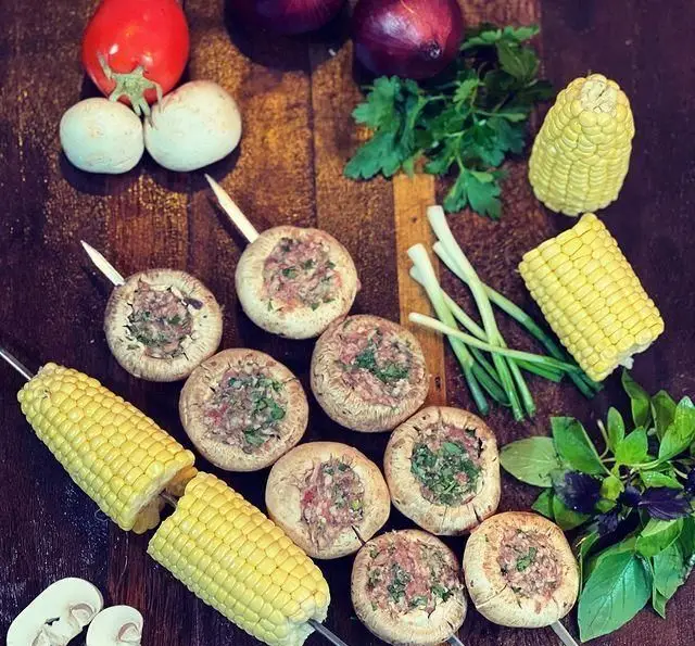 تصویری از مواد اولیه تازه و آماده سازی برای کباب در جگر سرای عیاران شامل قارچ شکم پر با گوشت، ذرت، پیاز، گوجه و سبزیجات.