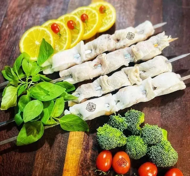 سیخ‌های کباب جگر و دل و قلوه تازه "عیاران" با لیمو، ریحان، بروکلی و گوجه گیلاسی آماده برای سرو. لذت غذای سنتی ایرانی و کبابی.