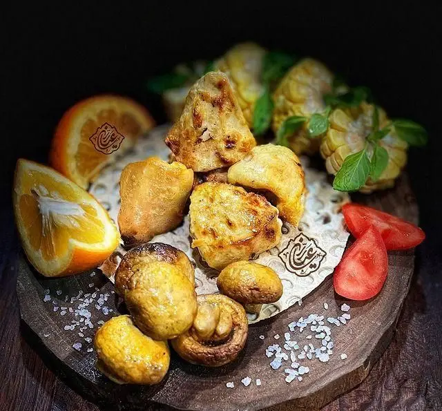 سینی کباب ویژه جگر سرای عیاران: تکه‌های مرغ و قارچ کبابی، همراه با پرتقال، ذرت تازه و گوجه فرنگی، غذایی خوشمزه و اشتهاآور.