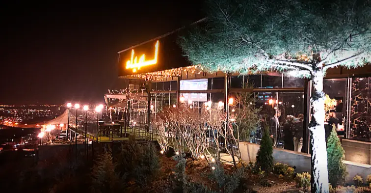 کافه رستوران لمیاء در شب، تابلوی نورانی، تراس با فضای باز و نورپردازی جذاب، چشم‌انداز خیره‌کننده شهر، تجربه‌ای فراموش‌نشدنی.