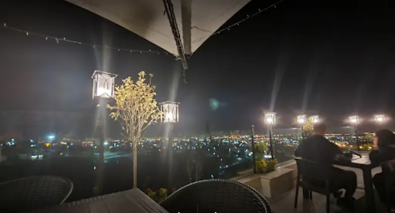 کافه رستوران لمیاء: منظره شب شهر از فضای باز روف گاردن، چراغ‌های روشن و میزهای چیده شده برای مشتریان.