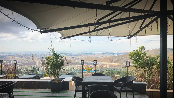 کافه رستوران لمیاء: فضای دلباز تراس با چتر سایبان بزرگ، میز و صندلی‌های شیک و چشم‌انداز بی‌نظیر شهر و کوهستان در پس‌زمینه.