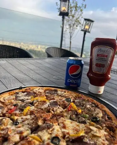 لذت پیتزای کافه رستوران لمیاء با تاپینگ‌های متنوع، نوشابه پپسی و کچاپ، در محیطی دلنشین و فضای باز با منظره‌ای تماشایی.