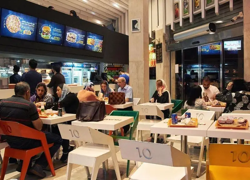تصویری از فضای داخلی شلوغ رستوران و فست فود پیتزا علیرضا منصوریان، با مشتریان در حال لذت بردن از غذا و منو دیجیتال متنوع