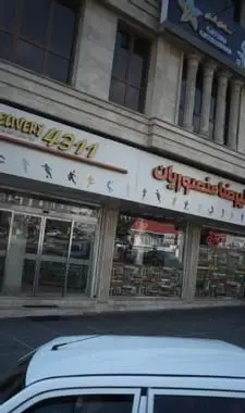 تصویر نمای بیرونی رستوران پیتزا علیرضا منصوریان، با تابلوی بزرگ و روشن، شماره دلیوری ۴۳۱۱ و نمادهای ورزشی.