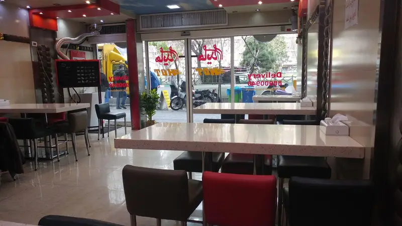 فضای داخلی تمیز و دلباز ساندویچ هایدا، با چیدمان میز و صندلی‌های مدرن، و ورودی شیشه‌ای مشرف به خیابان برای راحتی مشتریان.