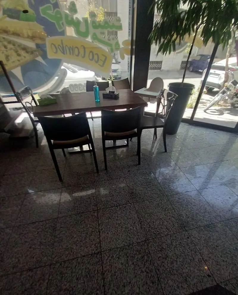 نمای داخلی رستوران پیتزا سیب ۳۶۰ با میز و صندلی، بطری آبی، دستمال کاغذی و پنجره‌ای بزرگ با لوگوی Eco Combo و منظره شهر.