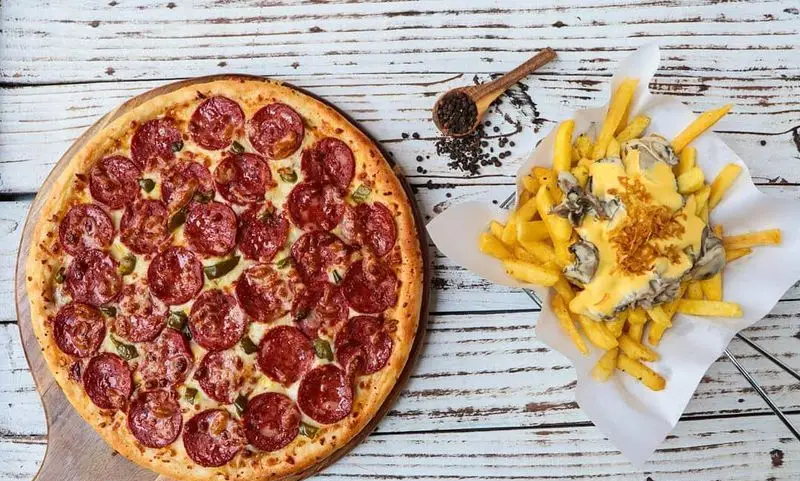 پیتزا پپرونی با فلفل سبز و سیب‌زمینی سرخ‌کرده پنیری و کرانچی مخصوص فست‌فود شیلا روی میز چوبی. بهترین انتخاب برای یک وعده لذیذ.