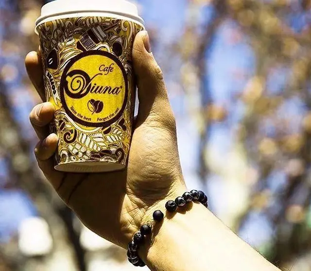 نمای نزدیک از فنجان قهوه برند کافه ویونا پلاس در دست، با طراحی منحصربه‌فرد و شعار "Taste the best Forget the rest".