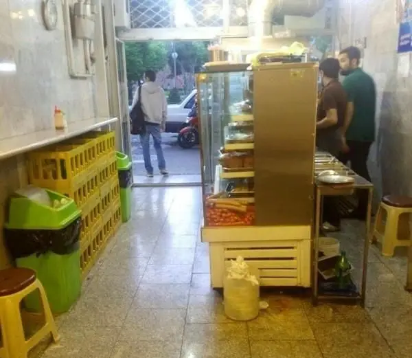 تصویری از داخل ساندویچی اغذیه فرد بلوار، شامل ویترین غذا، پرسنل مشغول کار و ورودی خیابان با مشتری.
