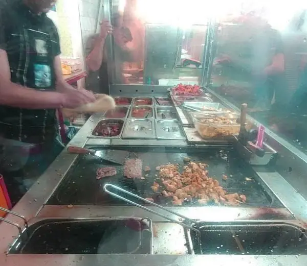 آشپز در ساندویچی اغذیه فرد بلوار مشغول آماده‌سازی ساندویچ، پخت گوشت و مرغ روی گریل و چیدن مخلفات تازه برای مشتریان.