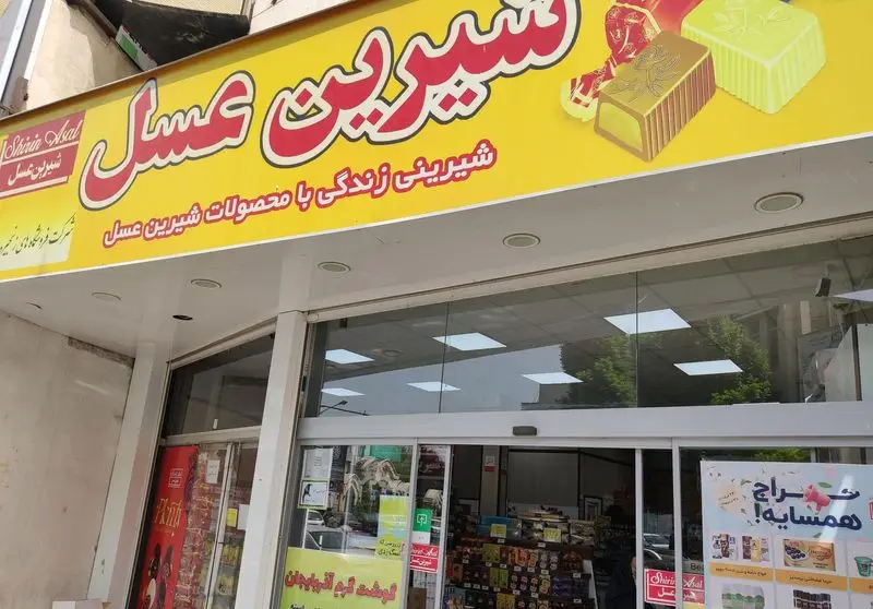 تصویری از نمای بیرونی فروشگاه بزرگ و مدرن شیرین عسل، با تابلوی جذاب و محصولات متنوع شکلات و شیرینی‌های مرغوب این برند معتبر.