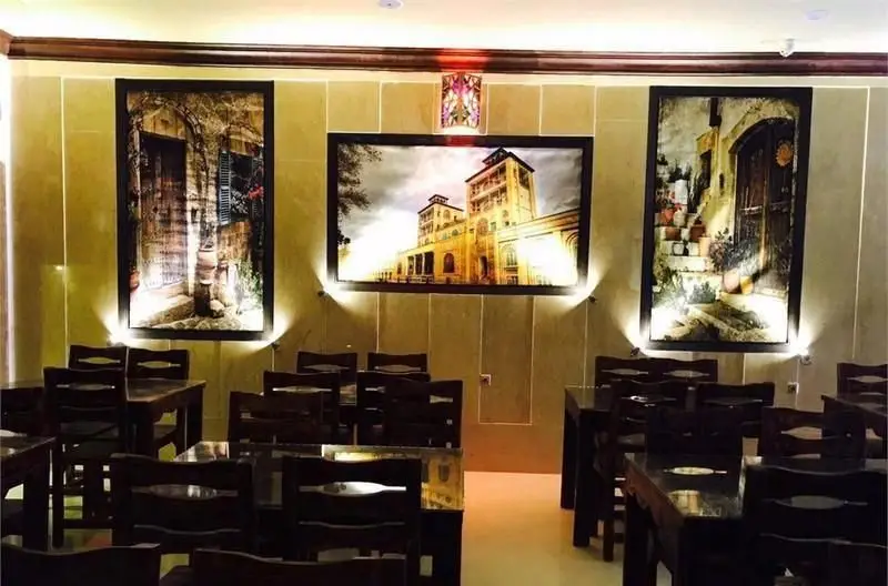 تصویری از فضای داخلی دلنشین و زیبای رستوران ایرانی عمارت شمس با دکوراسیون سنتی، میز و صندلی‌های چوبی و تابلوهای دیواری نورپردازی شده.