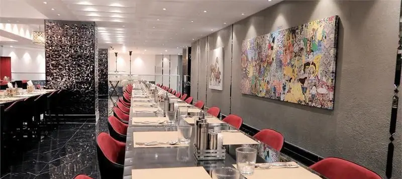رستوران ایرانی هانی، فضای پذیرایی شیک با میز طویل آماده سرویس‌دهی، صندلی‌های مخملی قرمز و دکوراسیون مدرن با اثر هنری خاص.