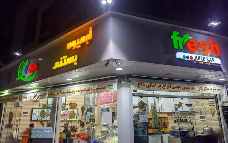 نمای شب آبمیوه بستنی لئون با تابلوهای روشن و کلمات fresh و juice bar به همراه آبمیوه و بستنی در ویترین مغازه