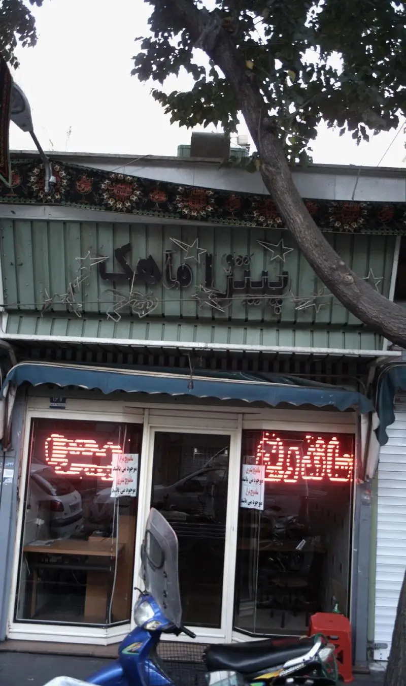 نمای بیرونی روشن و پر جنب و جوش کسب و کار فست فود پیتزا ماهک با تابلوی نئون جذاب و موتورسیکلت در جلوی مغازه، ارائه دهنده انواع پیتزا و ساندویچ خوشمزه